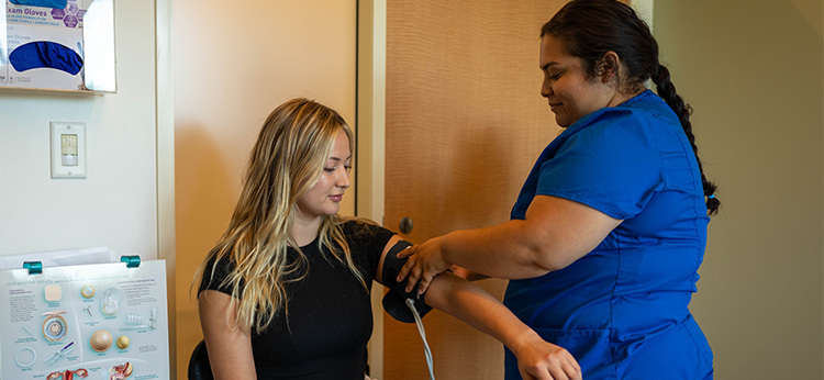 A female nurse wearing blue scrubs takes the blood pressure of a female student in the Student Health Services offices at Santa Rosa Junior College.