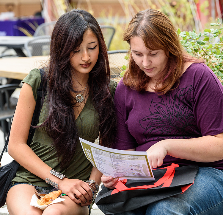 Two women seated outdoors on the Petaluma campus of Santa Rosa Junior College are looking at a list