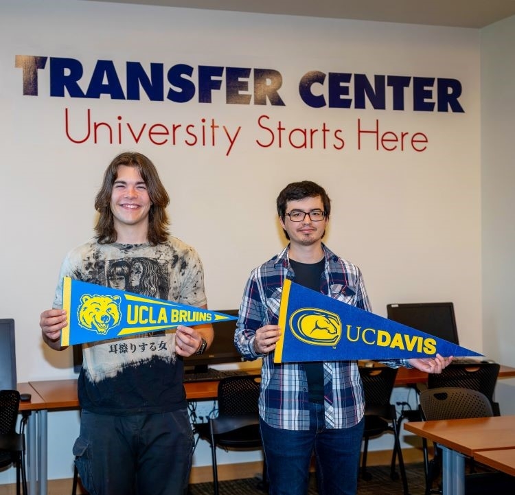 Two young male students pose and smile to the camera while holding with UCLA and UC Davis pennants in the Transfer Center at Santa Rosa Junior College. 