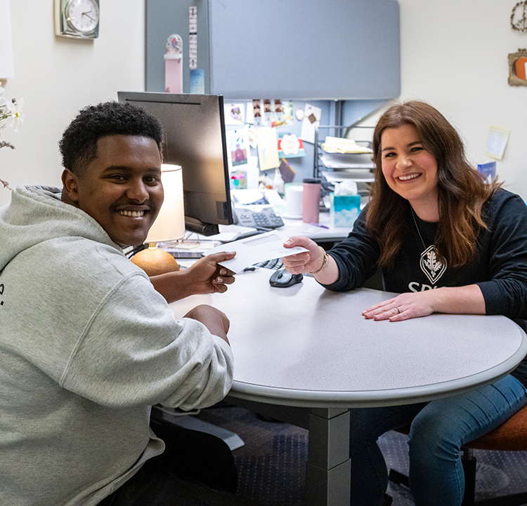 A male student receives a white envelope from a female staff member in the Financial Aid Offices at Santa Rosa Junior College.