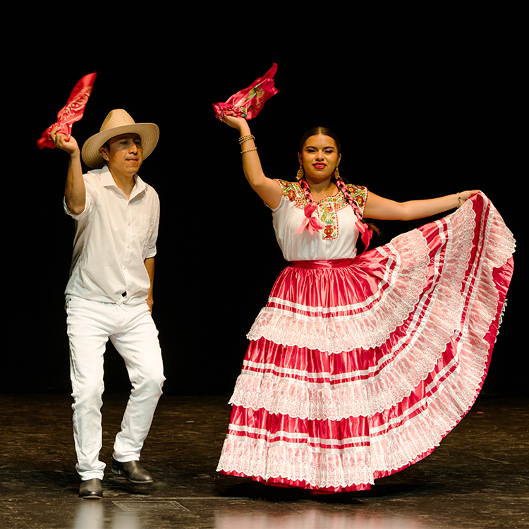 A male and a female wearing traditional Mexican attire are dancing on a stage at Santa Rosa Junior College. 