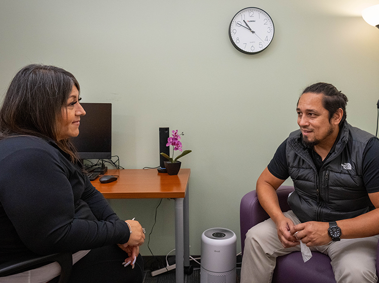 A Latinx young man speaks to a Native American woman therapist in a private room at the SRJC Student Psychological Services.