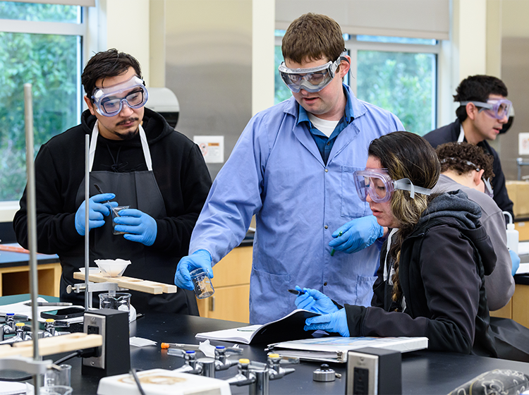 Two students wearing protective equipment listen to a lab assistant during a chemistry class at SRJC Petaluma 