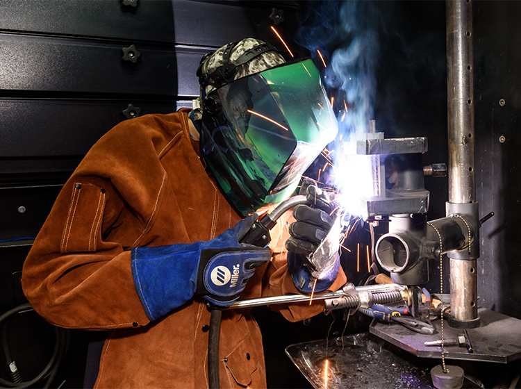 A welder wearing brown leather coveralls and welding protection equipment works in a career education lab at Santa Rosa Junior College.