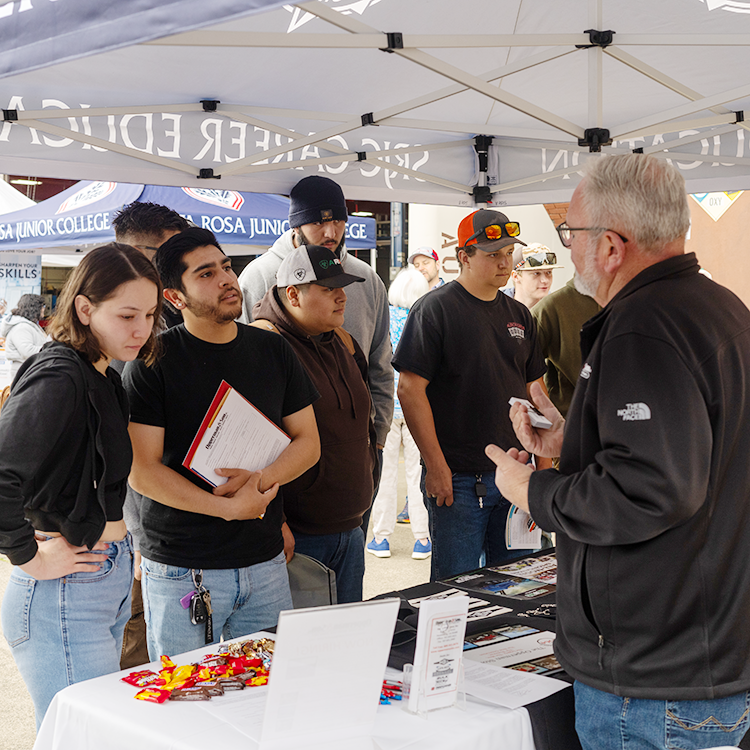 Young male and female students talk to employers under a canopy during the 2024 Industrial Trade Job Fair at Santa Rosa Junior College.